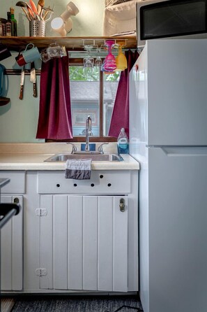 A compact kitchen with a sink, a refrigerator, and a window with curtains.