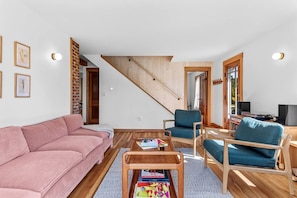Ein Wohnzimmer mit einem rosa Sofa, einem Holztisch, blauen Sesseln und einer Treppe.