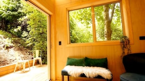 A wooden interior with a bench, a window, and a view of a forest.