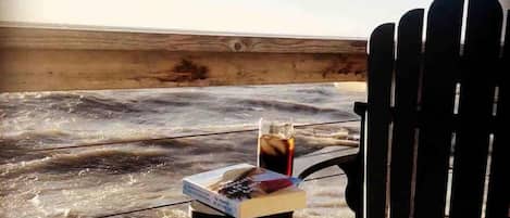 A chair facing a beach with a table holding a drink and a book.
