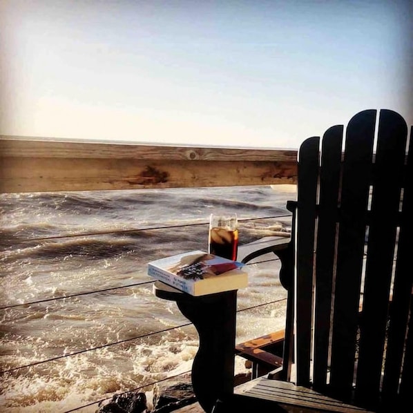 A chair facing a beach with a table holding a drink and a book.