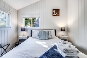 A bedroom with a bed, two bedside tables, a window, and a wall-mounted artwork.