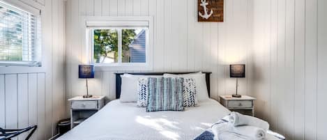A bedroom with a bed, two bedside tables, a window, and a wall-mounted artwork.