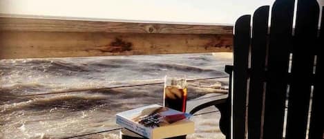 A chair facing a beach with a table holding a drink and a book.