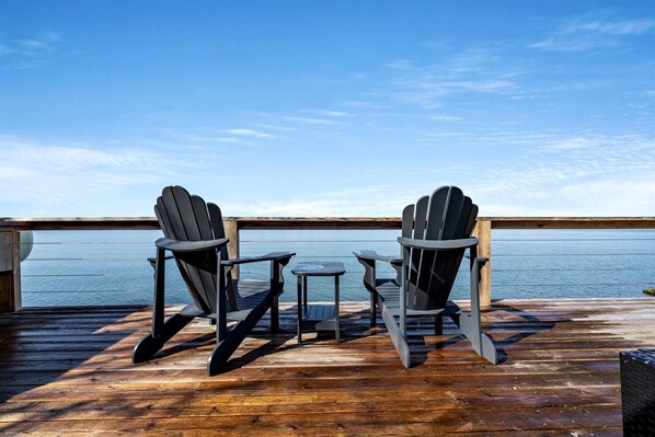 A deck with two Adirondack chairs and a small table, overlooking a body of water.