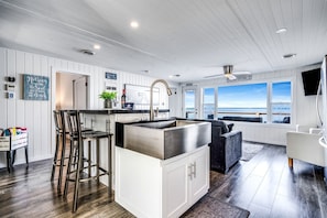 A modern kitchen with a bar area, white cabinetry, and a view of the beach.