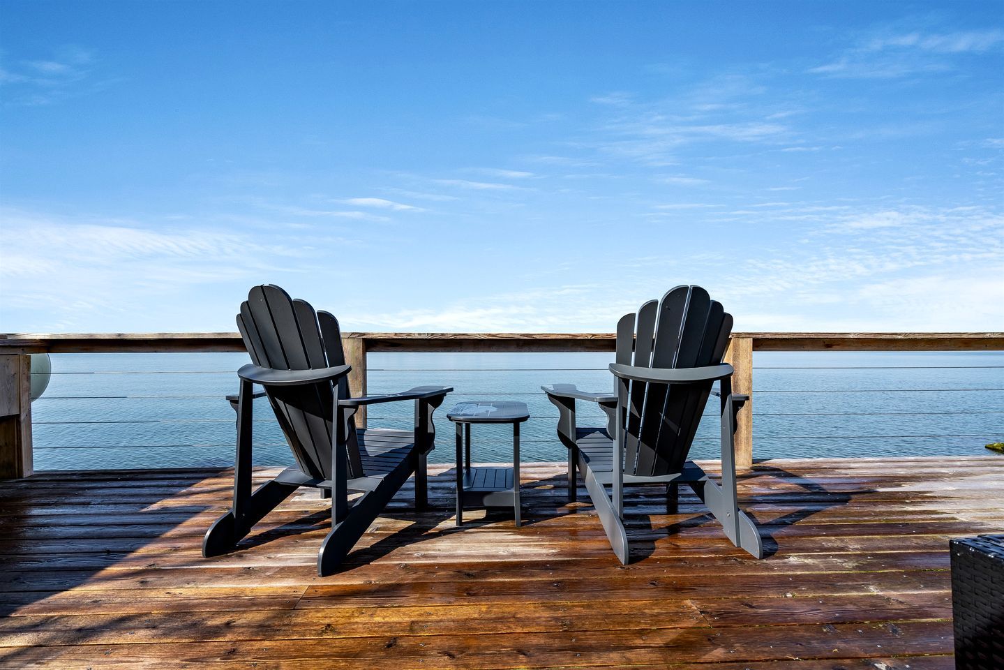 Una terraza con dos sillas Adirondack y una pequeña mesa, con vista a un cuerpo de agua.
