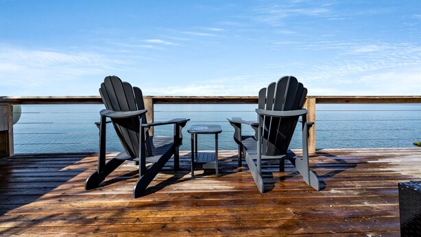Una terraza con dos sillas Adirondack y una pequeña mesa, con vista a un cuerpo de agua.