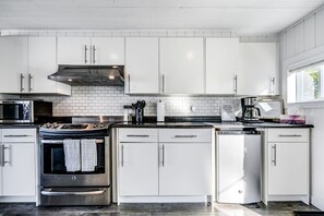 A modern kitchen with white cabinets, a stainless steel stove, and a coffee maker.