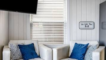 Un salon moderne avec deux canapés en cuir blanc, un téléviseur à écran plat et un panneau décoratif fixé au mur.