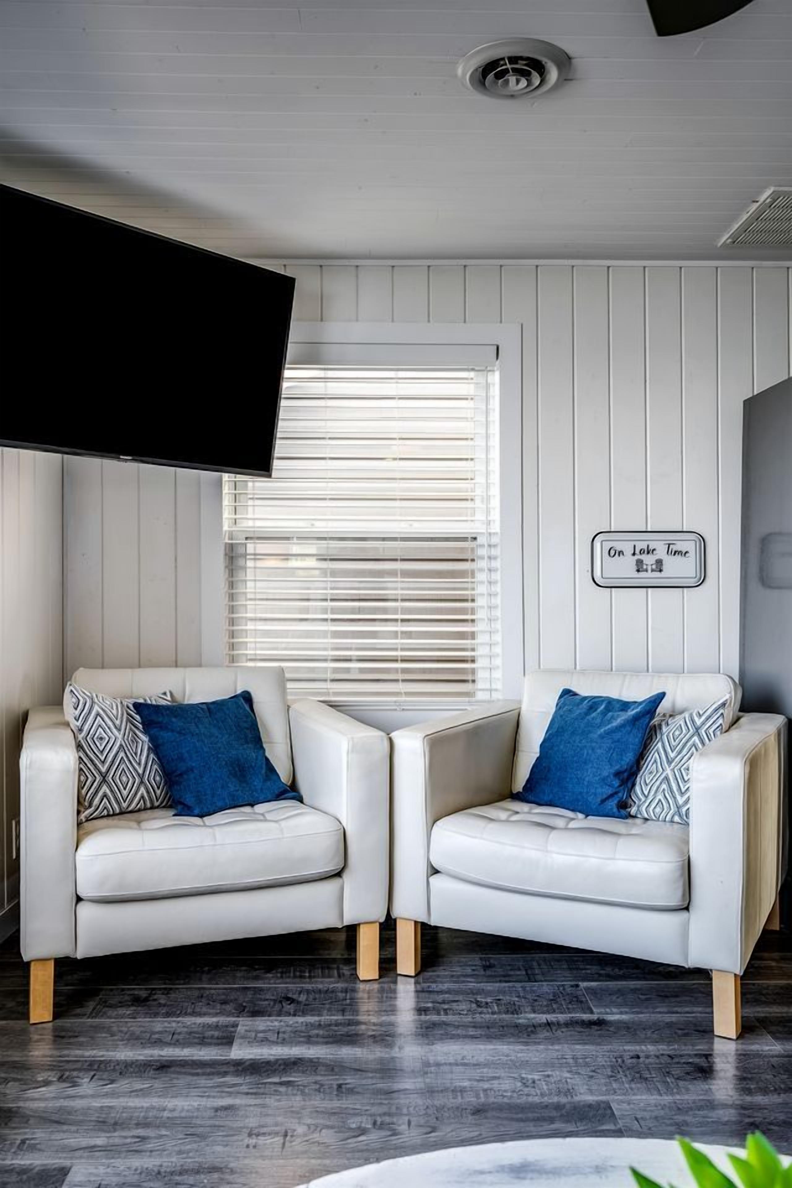 A modern living room with two white leather sofas, a flat-screen TV, and a wall-mounted sign.