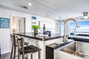 A kitchen with a bar area, a view of the beach, and a sign indicating a beach location. - Sweet Beach Rental with Jacuzzi, Deck and Amazing Sunsets in Ontario (Leamington)