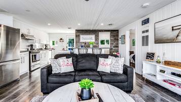 A modern kitchen with stainless steel appliances, a dining area with a black leather couch, and a living room with a white coffee table.