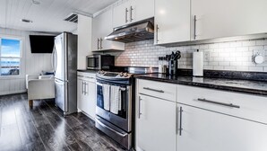 Una cocina moderna con muebles blancos, electrodomésticos de acero inoxidable, encimera negra y vistas al exterior a través de un ventanal.