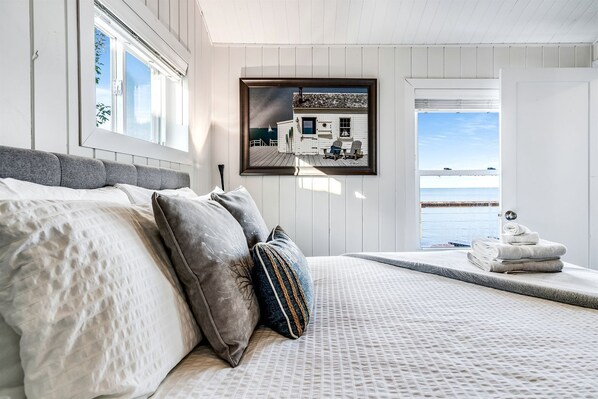 A bedroom with a bed, pillows, a framed picture, and a view of the sea. - Sweet Beach Rental with Jacuzzi, Deck and Amazing Sunsets in Ontario (Leamington)