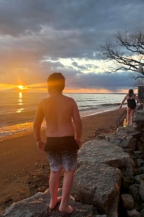 A beach scene with a sunset, rocky shoreline, and a person walking. - Sweet Beach Rental with Jacuzzi, Deck and Amazing Sunsets in Ontario (Leamington)