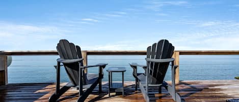 A deck with two Adirondack chairs and a small table, overlooking a body of water.