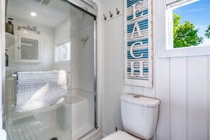 A bathroom with a glass shower enclosure, a white toilet, and a decorative sign with letters. - Sweet Beach Rental with Jacuzzi, Deck and Amazing Sunsets in Ontario (Leamington)
