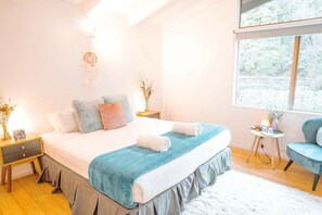 A bedroom with a bed, bedside tables, a chair, a window, and a view of trees.
