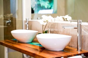 A bathroom with two white vessel sinks, a wooden vanity, a mirror, and a potted orchid.