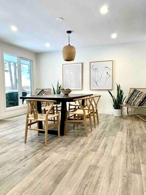 A dining area with a round table, wooden chairs, a hanging light fixture, and framed artwork on the walls. - Charming Cottage with Indoor Heated Pool near Sandbanks Provincial Park in Picton, Ontario (Prince Edward)