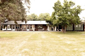 A building with a covered patio area, outdoor seating, and a lawn. - Charming Cottage with Indoor Heated Pool near Sandbanks Provincial Park in Picton, Ontario (Prince Edward)
