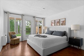 A bedroom with a large bed, a chair, a nightstand, and a view through the glass doors. - Charming Cottage with Indoor Heated Pool near Sandbanks Provincial Park in Picton, Ontario (Prince Edward)