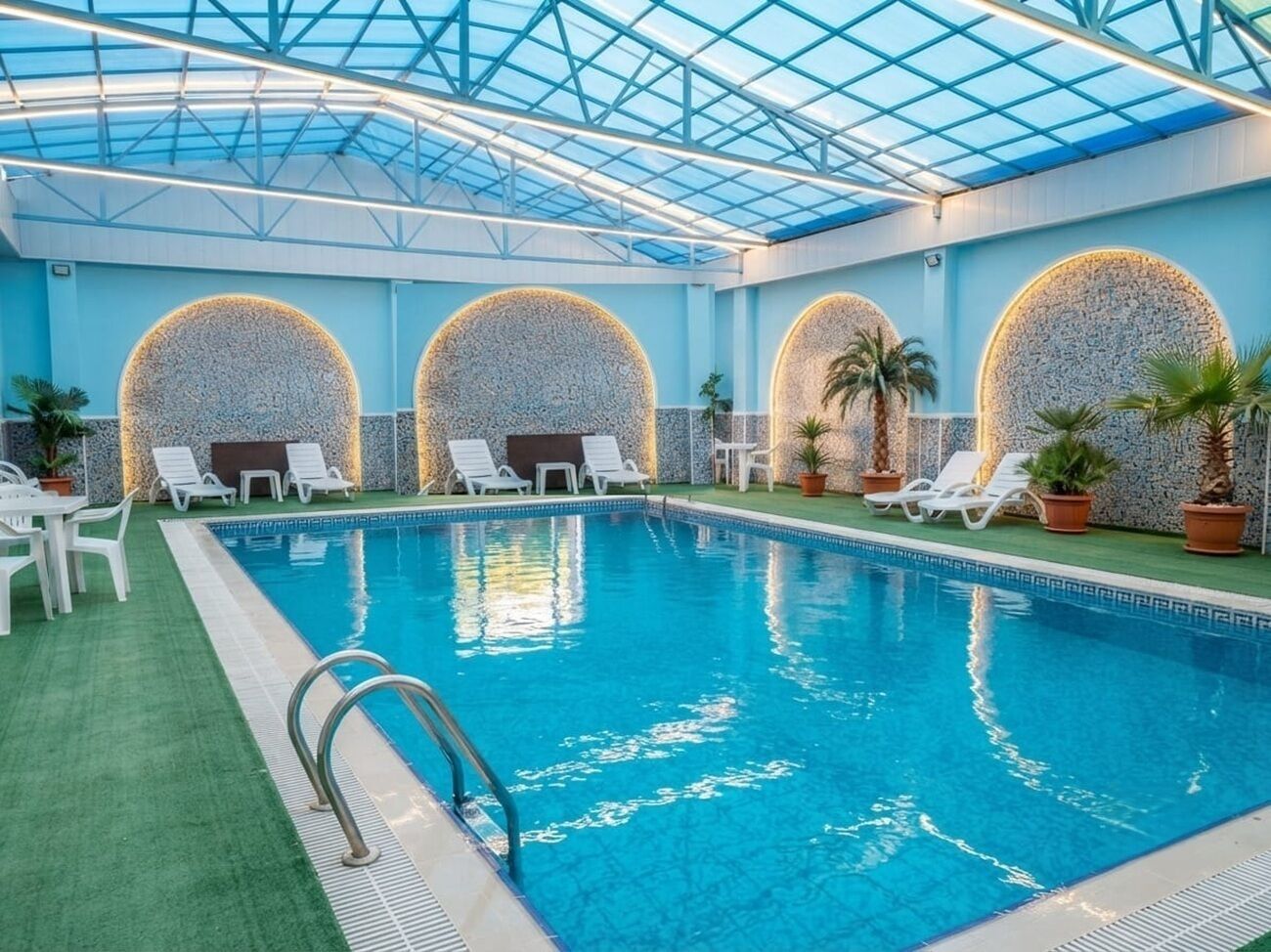 Uma piscina interior com teto de vidro, rodeada por espreguiçadeiras e plantas em vasos.