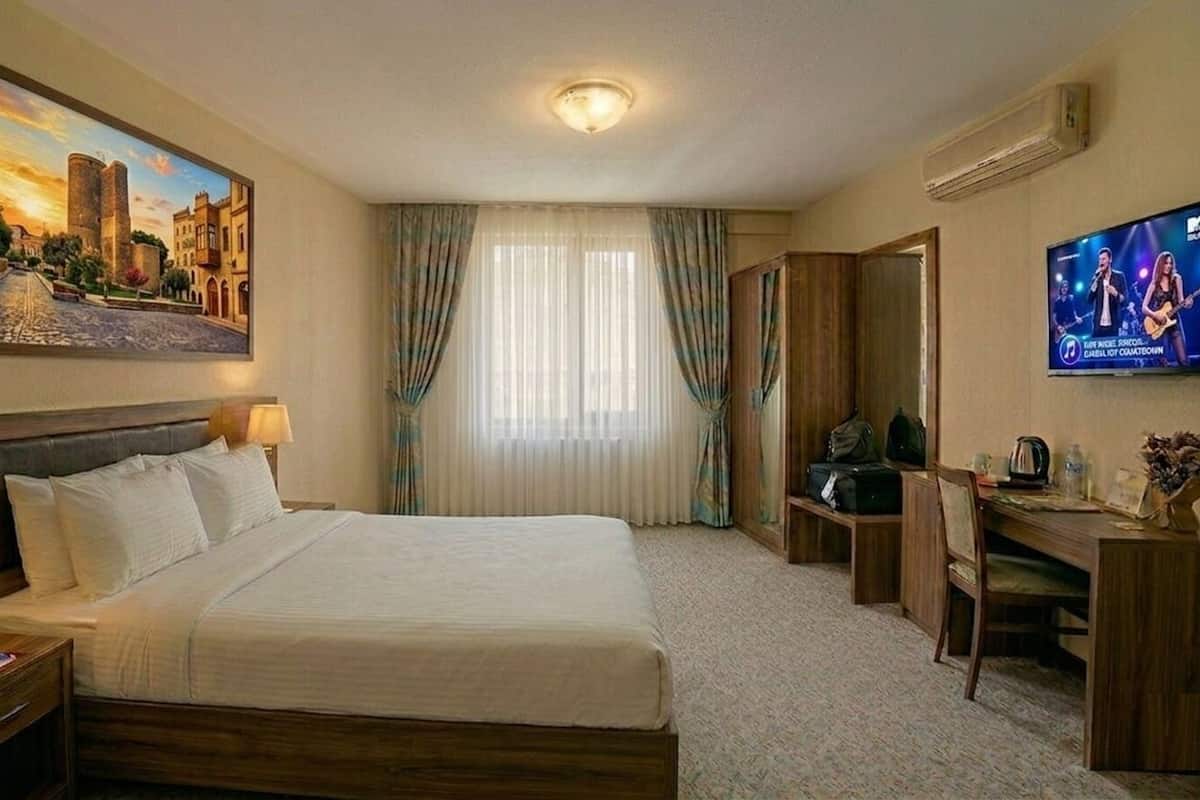Habitación de hotel con cama, mesitas de noche, escritorio, silla, televisor y un cuadro en la pared.
