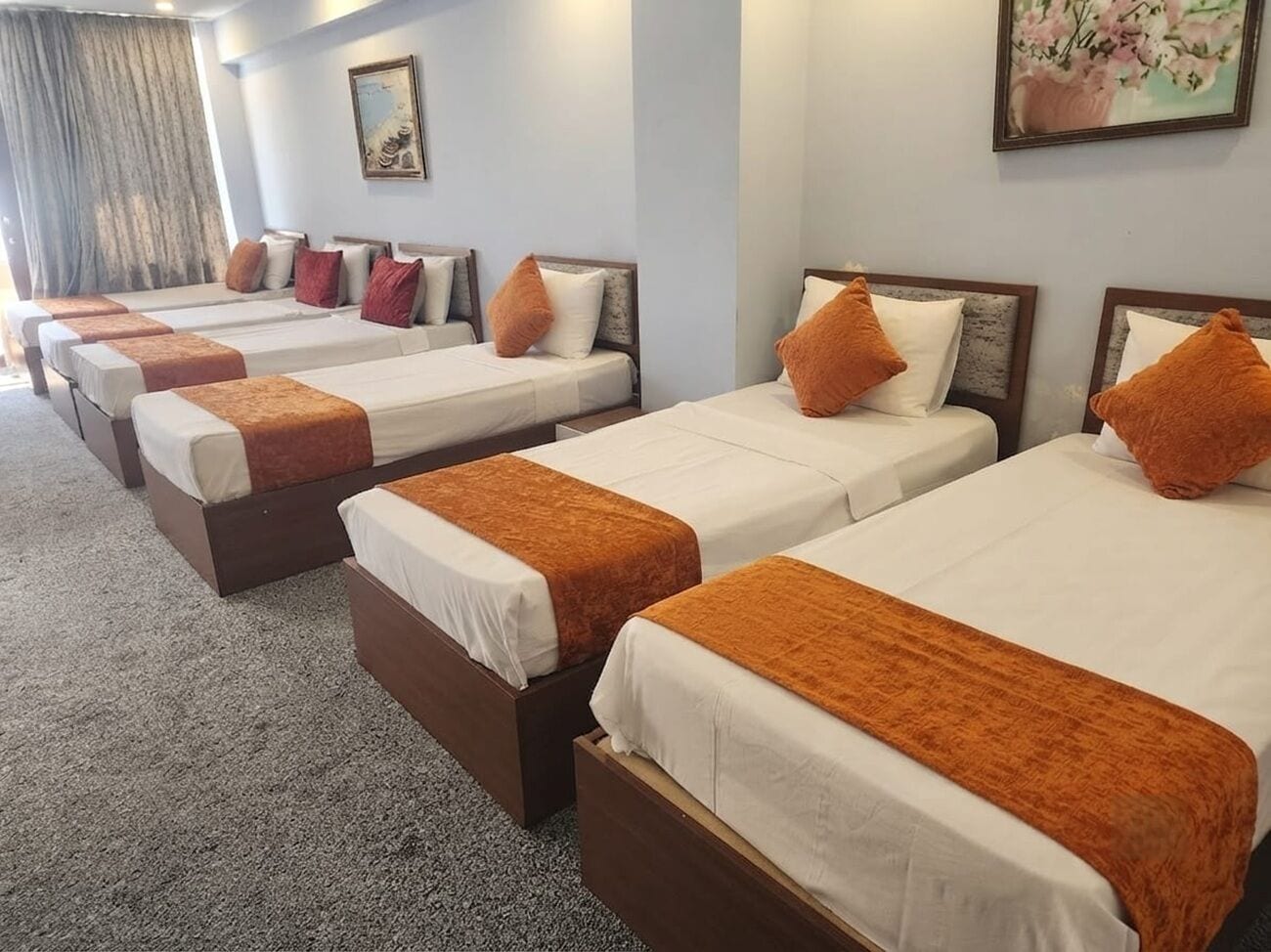 Ein Hotelzimmer mit vier Einzelbetten, die in einer Reihe angeordnet sind, jeweils mit einem Holz-Kopfteil und weißer Bettwäsche.