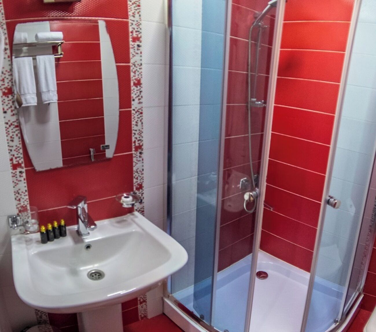 A bathroom with a white sink, a glass shower enclosure, and red and white tiled walls.