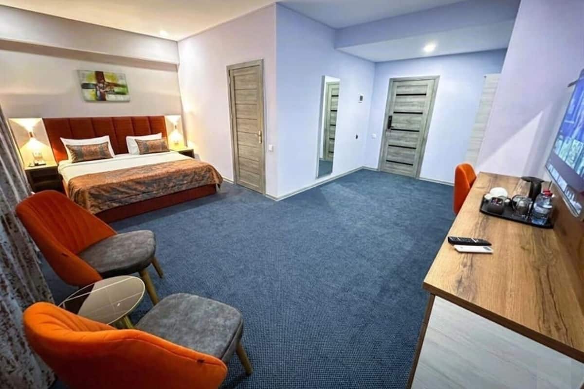 Habitación de hotel con cama, dos sillas, un escritorio con computadora y una mesita con una botella.
