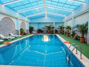 An indoor swimming pool with a glass ceiling, surrounded by lounge chairs and potted plants. - Amazon Hotel - Free Massage, Breakfast, & Dinner Included (Baku)