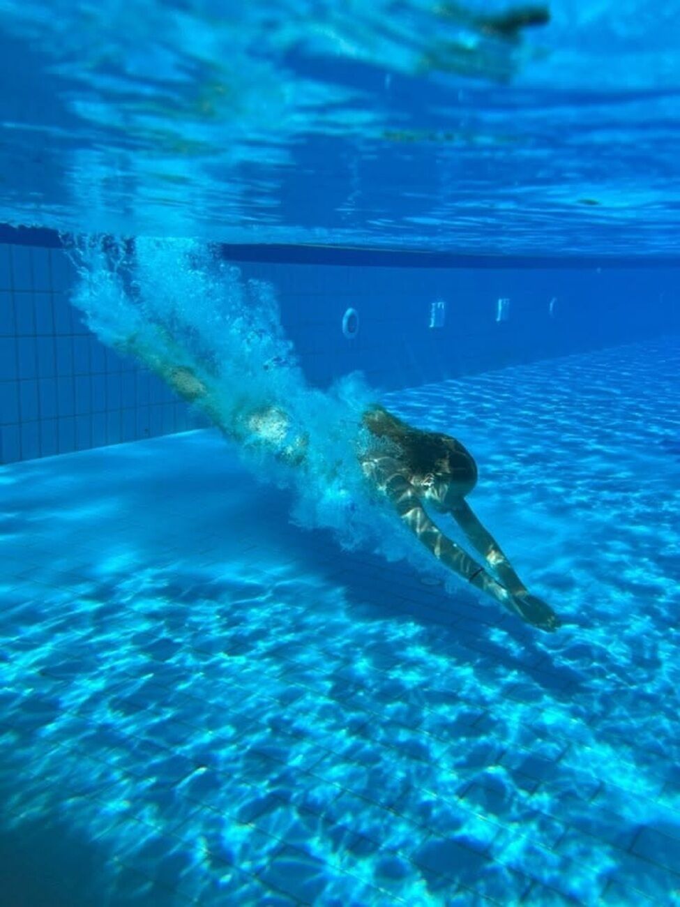 An underwater view of a swimming pool with a swimmer in motion.