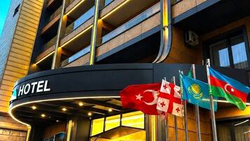 A hotel entrance with a red carpet leading to the door, multiple flags, and a modern building facade.