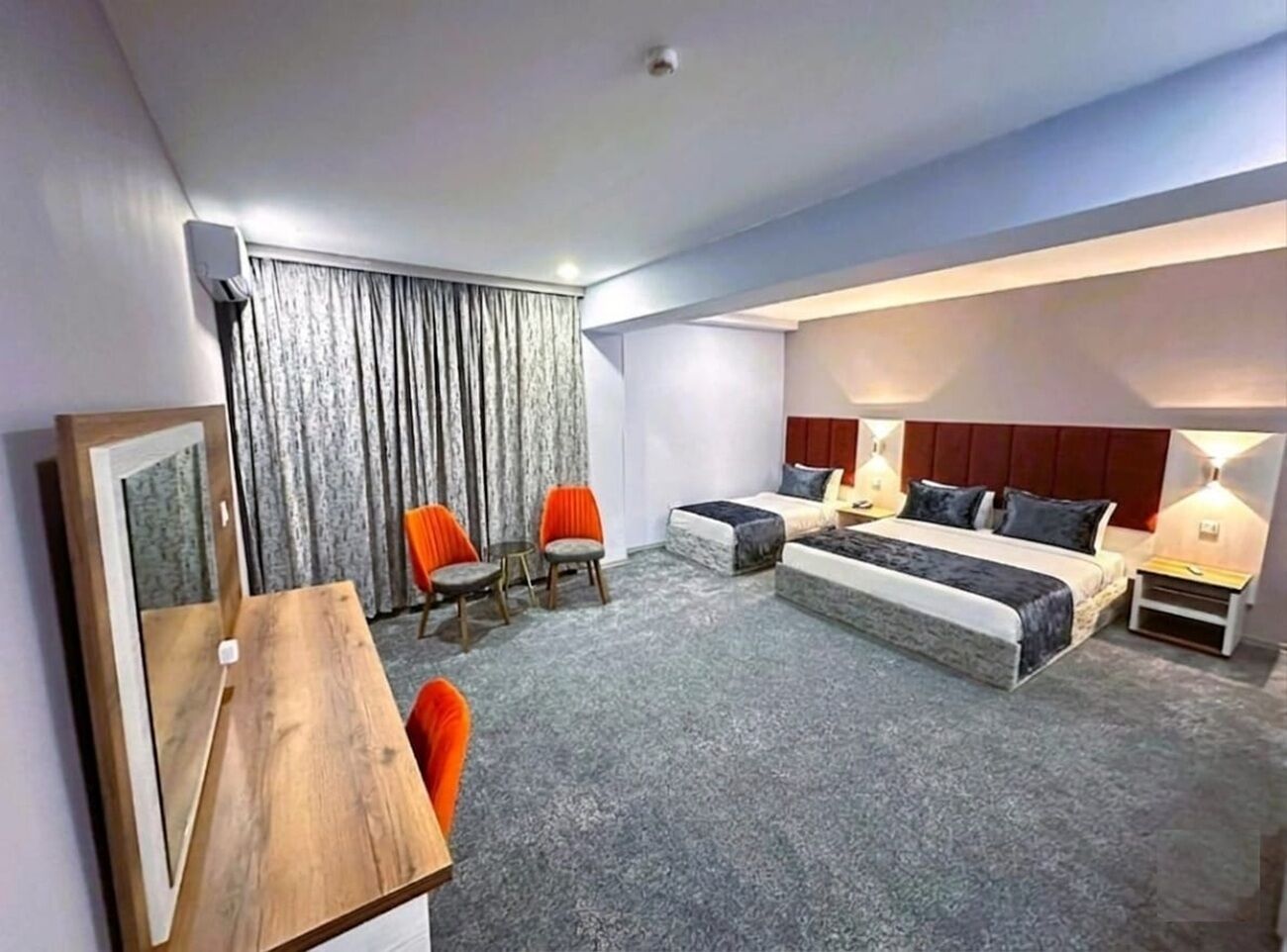 A hotel room with a bed, two chairs, a table, and a large window with curtains.