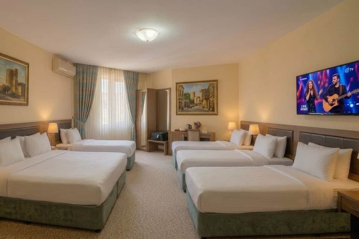 Habitación de hotel con dos camas, un escritorio, una silla, televisión y obras de arte en las paredes.