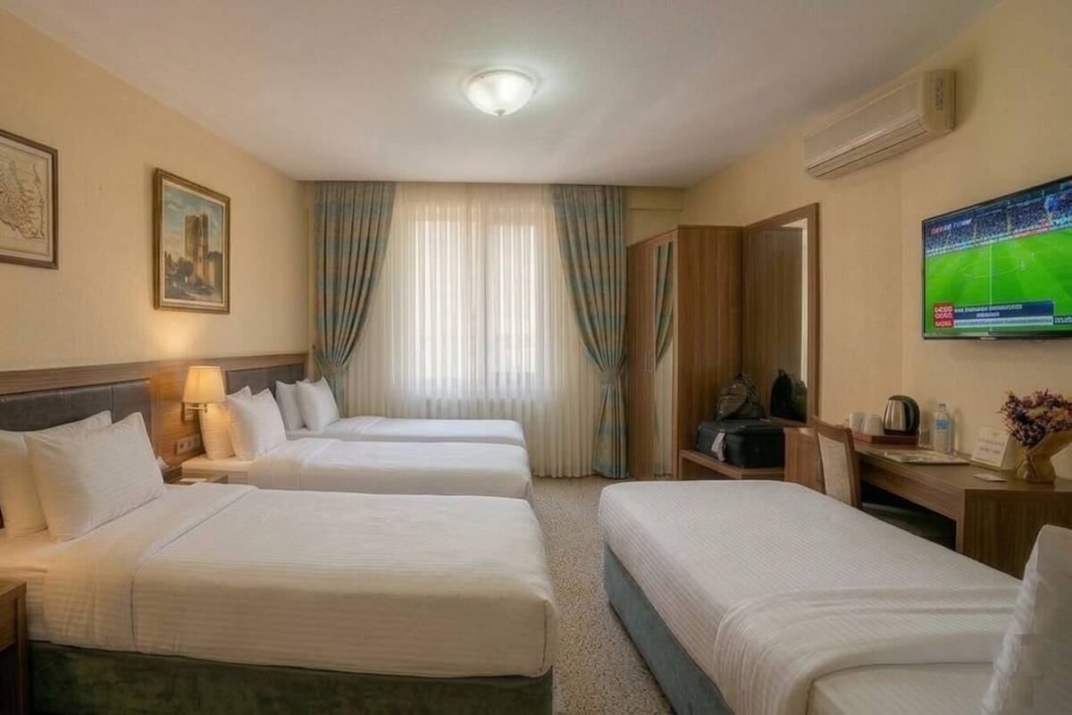 Habitación de hotel con tres camas, televisión, escritorio y ventana con cortinas.
