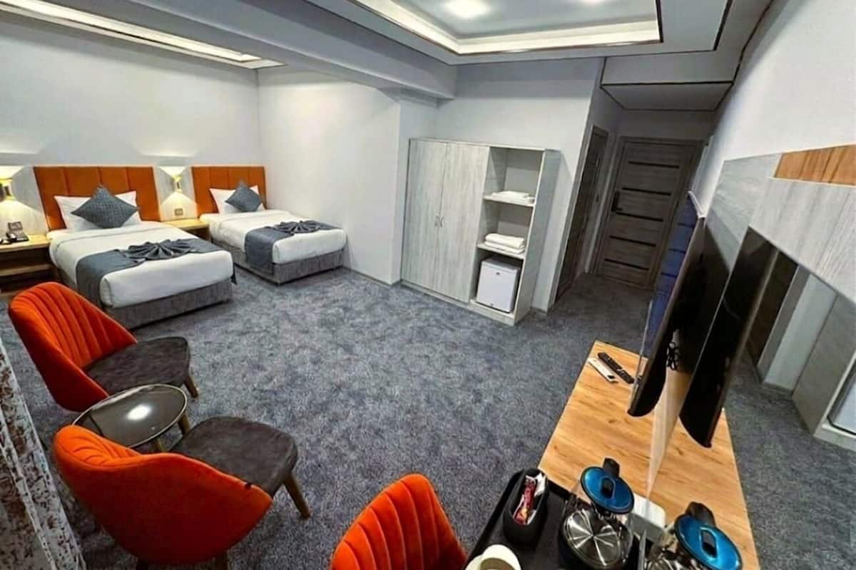 Habitación de hotel con dos camas, un escritorio, una silla, un armario y un televisor.