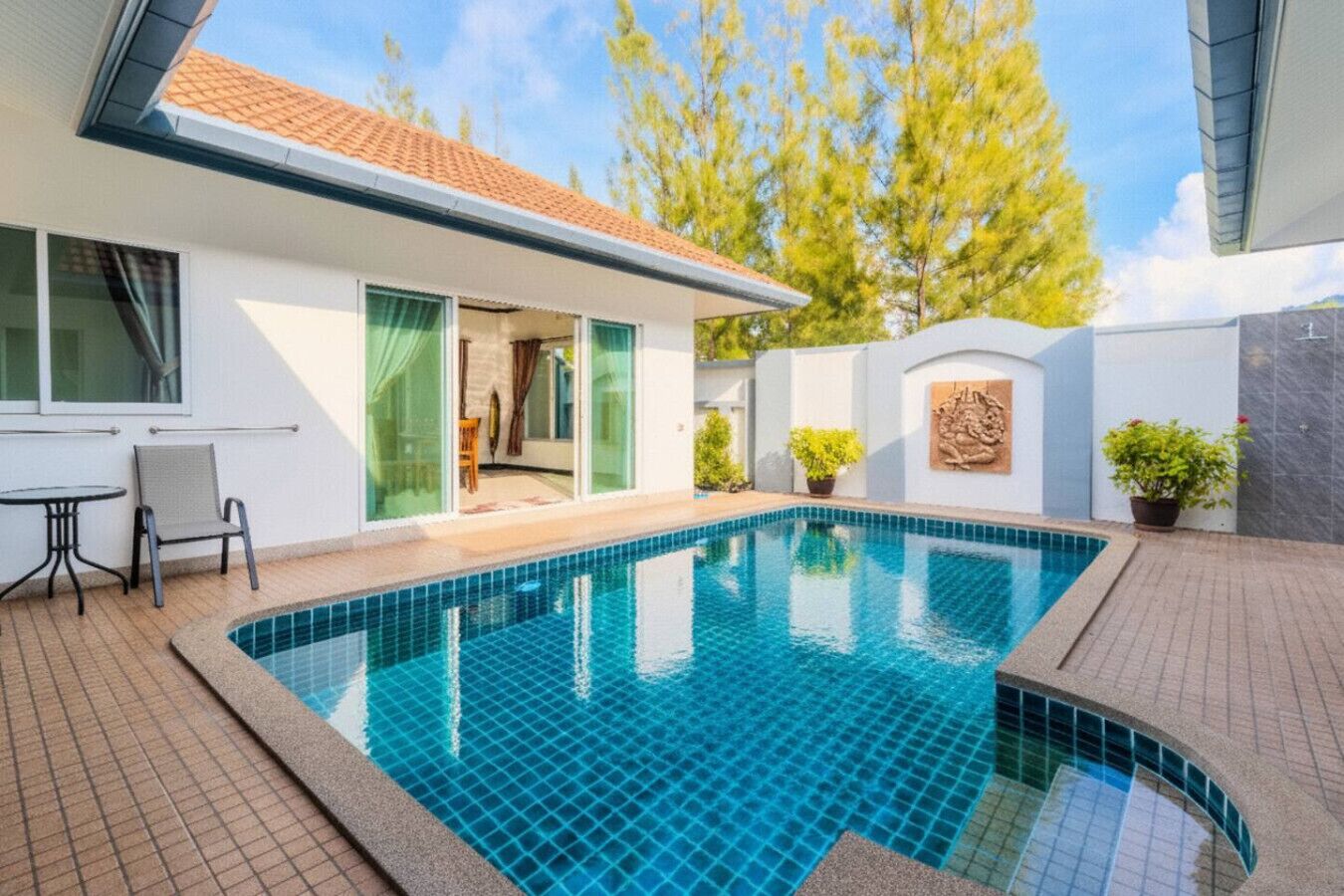 Een modern huis met een zwembad, een terras met een tafel en stoelen, en een deur naar een overdekt gedeelte.