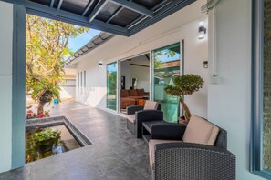 Ein überdachter Außenbereich mit Pool, Baum und Blick auf ein Haus.