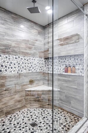 Une douche avec une porte en verre, un sol décoré de motifs de galets et une étagère pour les articles de toilette.