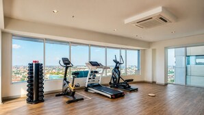 Un gimnasio espacioso con cinta de correr, elíptica y soporte para pesas, ventanas amplias con vista a la ciudad.
