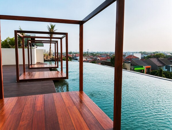A modern outdoor pool area with wooden decking and a view of the surrounding neighborhood. - Grand Kamala Lagoon Meeran By Reccoma (Bekasi)