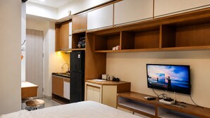 Habitación de hotel con cama, televisión, kitchenette y escritorio.