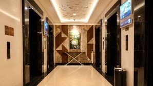 Un moderno vestíbulo de hotel con un muro de diseño geométrico, una pantalla digital y un cubo de basura.