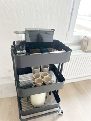 Een zwarte koffiemachine op een karretje met verschillende bekers en een kaars.
