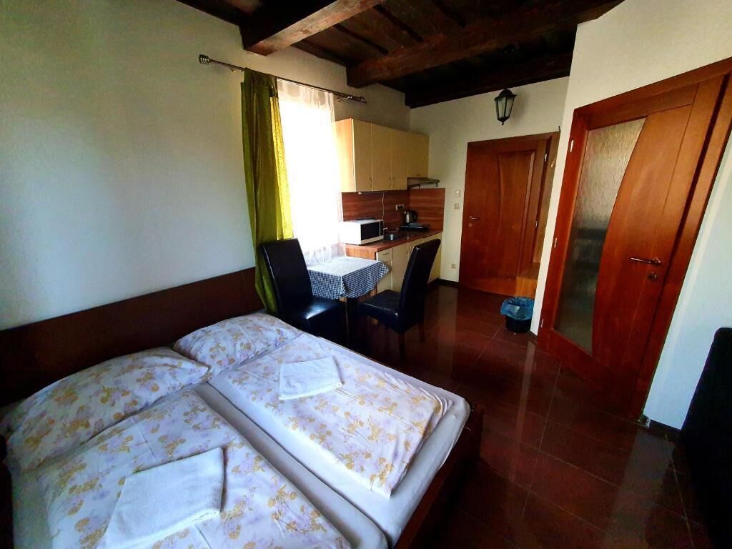 A room with a bed, a small table, chairs, a microwave, and a kitchen area.