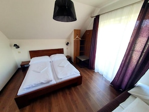 A bedroom with a wooden bed, a hanging wardrobe, and a bedside table.
