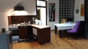 A compact kitchen with a stove, microwave, and cabinets, a dining table with chairs, and a window with a view. - Penzion U Adama (Dolná Tižina)